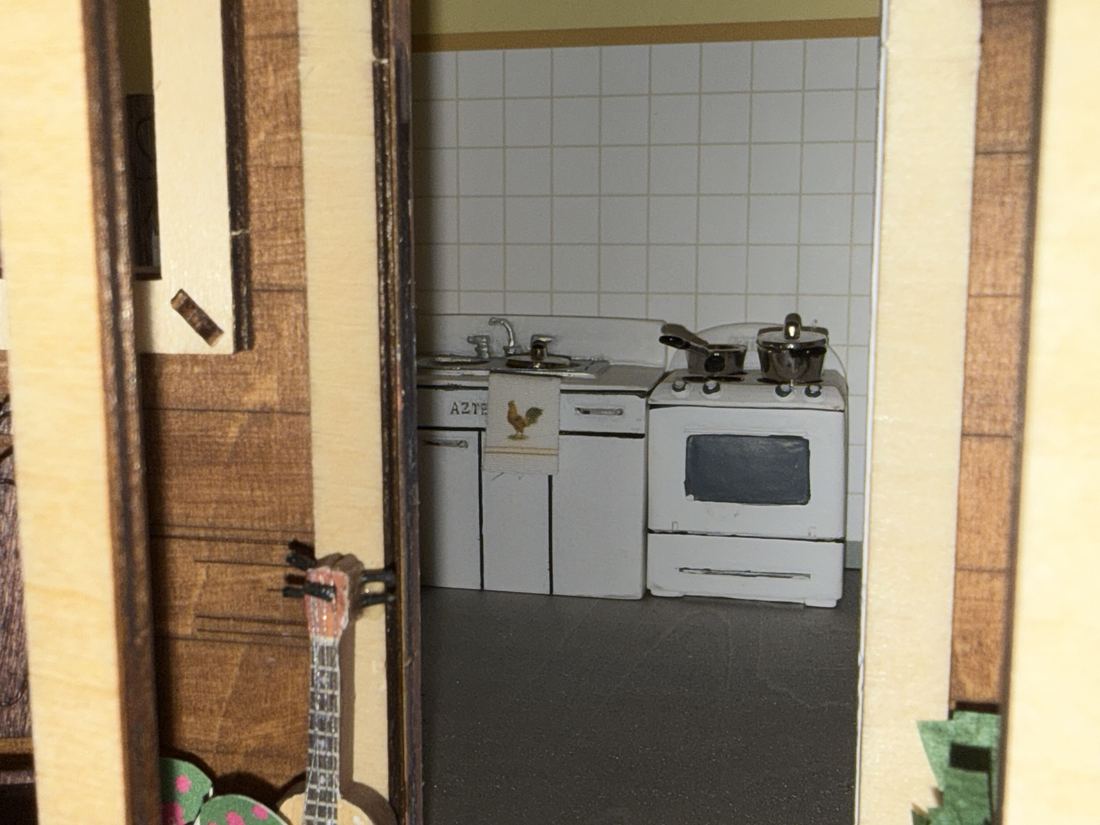 Close-up of the kitchen: white tile wall, sink cabinet with a rooster dish towel, and a white stove with two pots