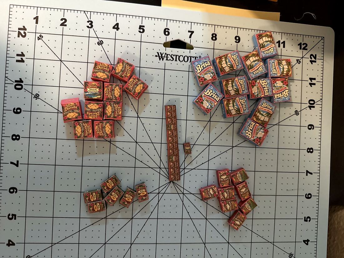 Folded and glued miniature grocery boxes grouped by brand on a cutting mat